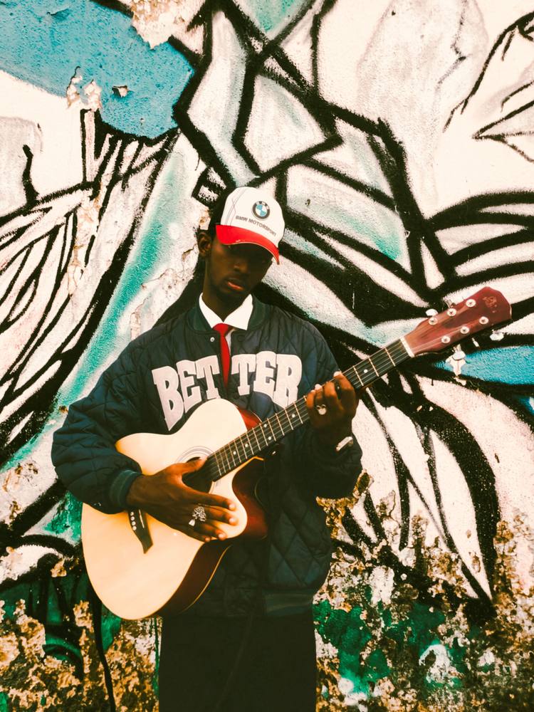 Musician playing guitar in front of a mural